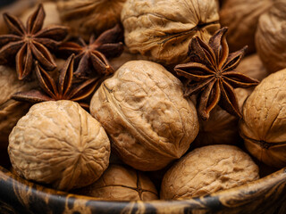 Closeup macro photo of healthy whole walnuts in shell with star anise spice in a wood bowl. 