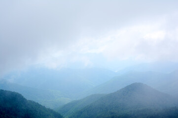 A mystical view of  green mountains partially concealed by thick, swirling fog, where glimpses of lush slopes emerge like islands in a sea of mist.