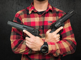A man in a red plaid flannel shirt stands against a dark background, holding two large powerful...
