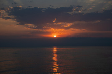 Dramatic golden sunrise over sea with breaking through dark clouds. Peaceful and serene horizon at dawn as the sun rises and reflects on calm water. Hope and new beginnings