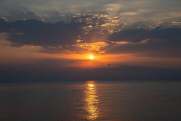 Obraz premium Dramatic golden sunrise over sea with breaking through dark clouds. Peaceful and serene horizon at dawn as the sun rises and reflects on calm water. Hope and new beginnings