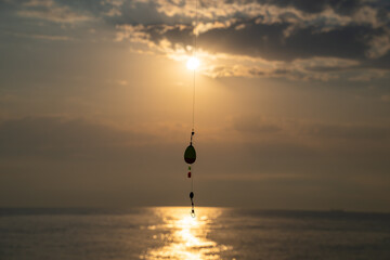 Fishing float hanging with sunset over the sea. Fishing line silhouette against golden sun with...