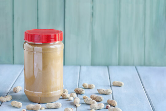 Front view of a full jar of peanut butter over a blue table with copy space and green background. Selective focus with blurred background.