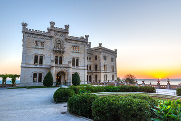 Obraz premium Castello di Miramare in Trieste, Italy, with the sun setting over the Adriatic Sea in the background