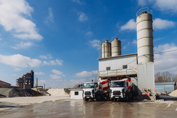 Concrete mixer trucks parked at production plant under blue sky