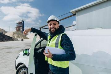 Smiling engineer holding blueprint at concrete production plant