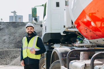 Construction engineer holding blueprint near cement truck in concrete production plant