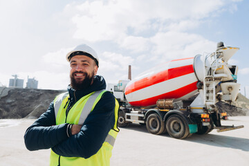 Construction worker smiling at concrete production plant with cement truck