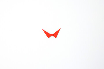 Symmetrical red paper fold bowtie on plain surface, ideal for origami tutorials, meditation brands, packaging design, children education, and minimalist lifestyle blogs. step in creative DIY project,