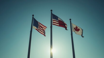 Three national flags, USA, Texas, Canada, waving in sunlight against a clear blue sky.