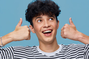 smiling man showing thumbs up wearing striped shirt against blue background, cheerful young adult...