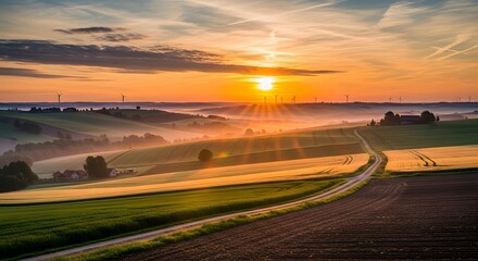 Golden sunrise illuminates rolling agricultural fields and misty valleys with distant industrial silhouettes