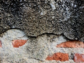 Black cement wall with peeling surface exposing red bricks inside