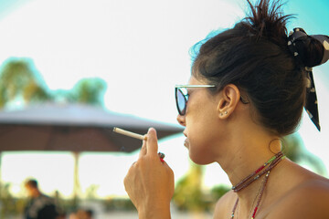 Beautiful brunette woman smokes a cigarette while looking at her cell phone. The woman is...