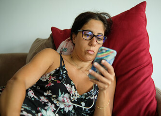 Beautiful brunette woman rests on the sofa looking at her cell phone. The woman is thirty-eight...