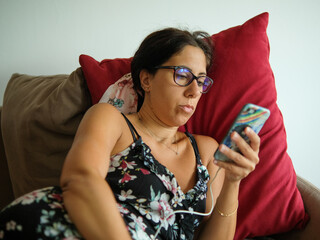 Beautiful brunette woman rests on the sofa looking at her cell phone. The woman is thirty-eight...