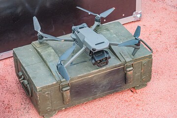 Small military-grade gray drone on green metal case with handle Indoor setting with artificial...