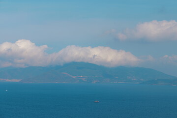 Scenic coastal landscape with a calm blue ocean and distant mountains under a cloudy sky. Tranquil seascape with a large island in the background.
