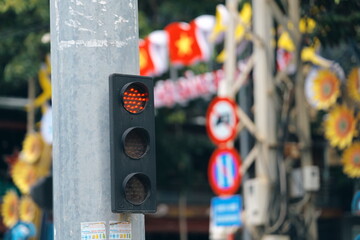 A red traffic light signaling stop on a city street pole. Out-of-focus background shows Vietnamese flags and road signs.