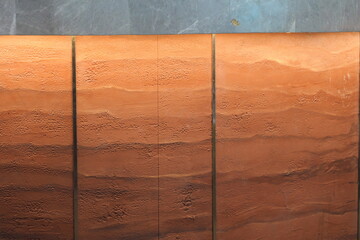 Modern interior wall with a textured rammed earth finish. Abstract background of layered terracotta...