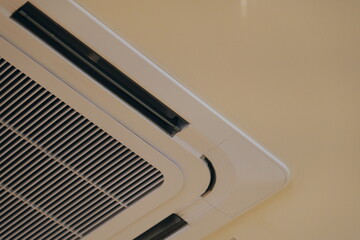 Close-up of a modern ceiling-mounted cassette air conditioner unit. HVAC system for cooling and ventilation in an office or home.