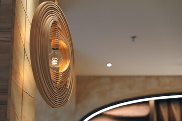 Modern wooden pendant lamp with a glowing Edison bulb. Stylish interior design element with warm,...