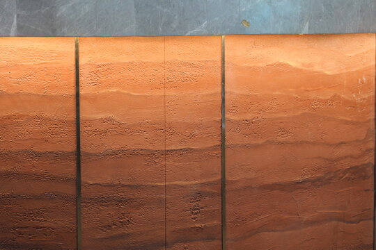 Modern interior wall with a textured rammed earth finish. Abstract background of layered terracotta plaster and grey marble.