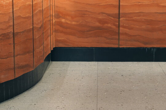 Modern interior architectural detail with a curved terracotta wall, black baseboard, and gray terrazzo tiled floor. Abstract background of building materials.