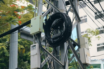 A complex tangle of electrical wires and communication cables on a metal utility pole. Urban...