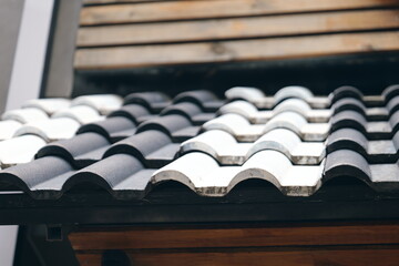 Architectural detail of a modern roof with a pattern of black and white curved ceramic tiles. Close-up of a building exterior.