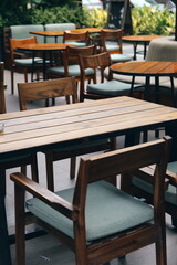 Empty wooden tables and chairs with green cushions at an outdoor cafe patio. Modern restaurant terrace furniture.