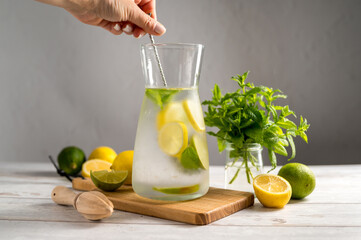 Female hand mixing lemonade with lemons, limes and fresh mint.