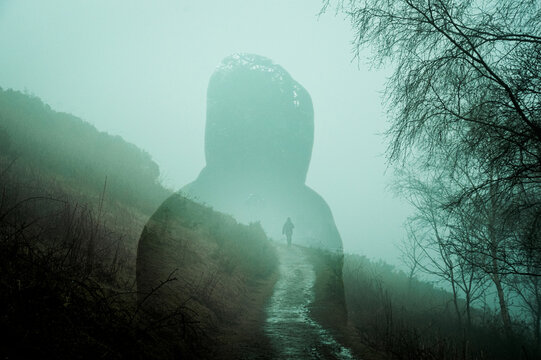 Hooded figure, with a spooky figure in the distance, walking along a path on a hill. On an eerie foggy winters day