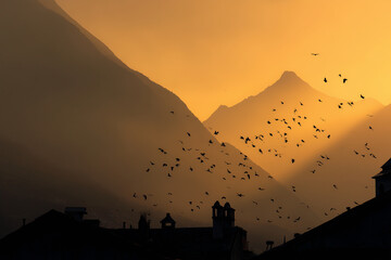 Fototapeta premium Bird Silhouettes at Sunset Over a Mountain Village