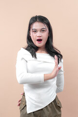 Young Asian woman with surprised expression raising hand in stop gesture, wearing casual white...