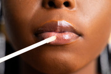 Close-up of an African woman applying lip gloss with a wand. Beauty, makeup detail.