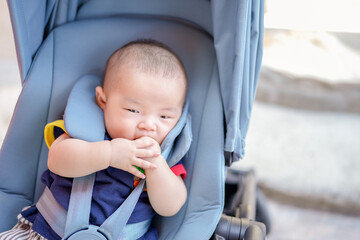 A baby is sitting in a stroller with a blue canopy. The baby is holding onto a toy and he is looking at something