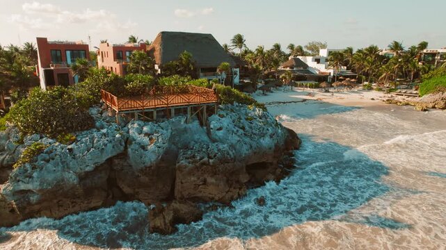 Woman on a wooden deck overlooking tropical resort scenic beach town with cliffside lookout and palm trees facing turquoise sea in Tulum, Mexico