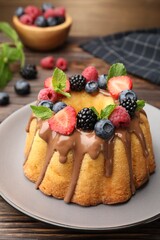 Tasty Bundt cake with berries, chocolate and mint on wooden table, closeup