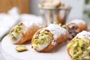 Delicious cannoli with ricotta cheese, pistachios and powdered sugar on table against blurred background, closeup