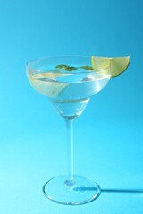 Martini cocktail with slices of lime and mint on light blue background, closeup