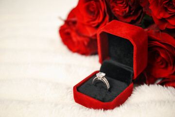 Dreams come true. Beautiful engagement ring in box and flowers on light plaid, closeup. Space for...