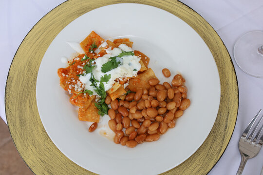 Top view of chilaquiles with beans (frijoles de la olla) on a white plate.