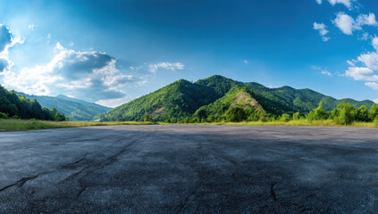 An open asphalt area with a beautiful mountainous landscape under a clear blue sky with scattered clouds.