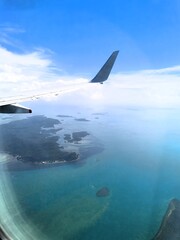 Airplane wing over turquoise ocean and islands under a blue sky