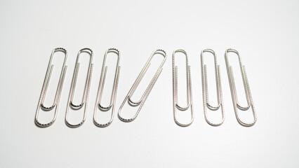 A close-up view of a row of seven silver paper clips on a clean white surface, with one clip at an angle.