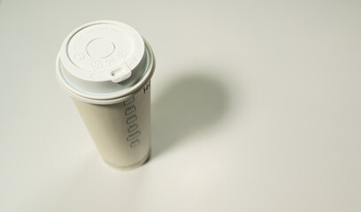 high-angle view of a neutral-colored paper coffee cup with a plastic lid, isolated on a white surface.