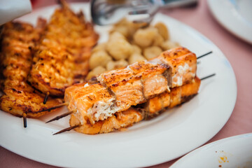 Delicious grilled salmon kebab on a white plate, restaurant cuisine, catering for events. Seafood shashlik, slices of salmon on a wooden skewers close-up, background with copy space