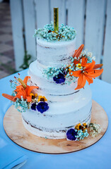 Three-tiered white wedding cake decorated with  orange, blue, yellow and white fresh flowers   on a wooden stand with fireworks on top