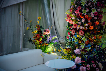 A cozy place next to a huge floral arrangement with a white sofa and a small white coffee table. A place for relaxation, reflection and talk at a party